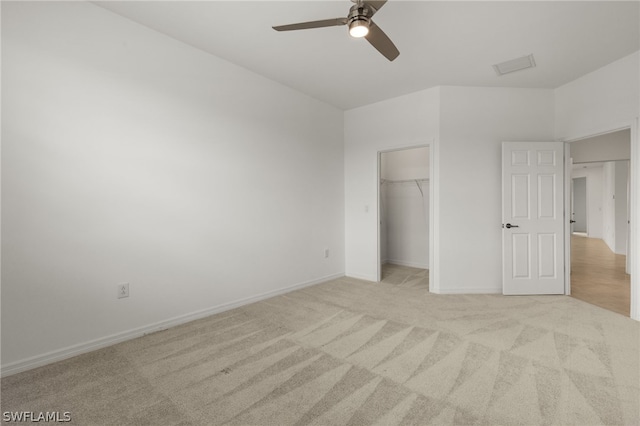 unfurnished bedroom featuring a walk in closet, a closet, ceiling fan, and light colored carpet