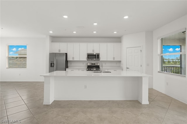 kitchen featuring a center island with sink, appliances with stainless steel finishes, white cabinetry, and light tile flooring