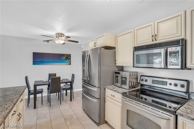 kitchen with light stone countertops, light tile flooring, appliances with stainless steel finishes, cream cabinetry, and ceiling fan