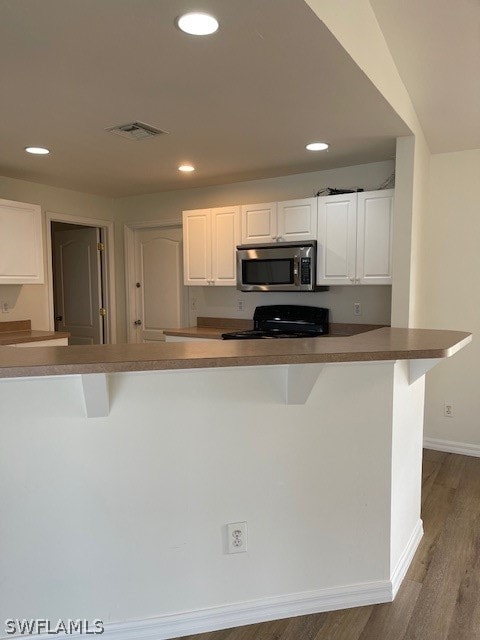 kitchen with stove, a breakfast bar area, white cabinetry, and wood-type flooring