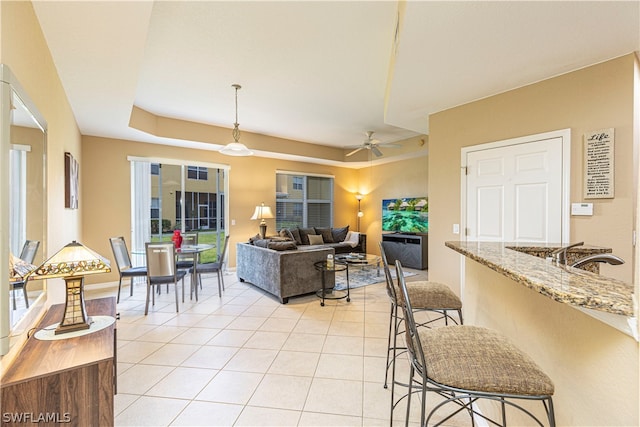 living room featuring sink, ceiling fan, light tile floors, and a raised ceiling