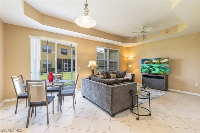 living room with a raised ceiling, ceiling fan, and light tile floors