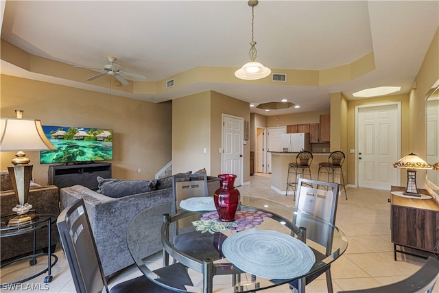 tiled dining area with ceiling fan and a raised ceiling