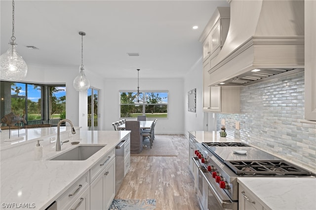 kitchen with premium range hood, appliances with stainless steel finishes, hanging light fixtures, tasteful backsplash, and sink