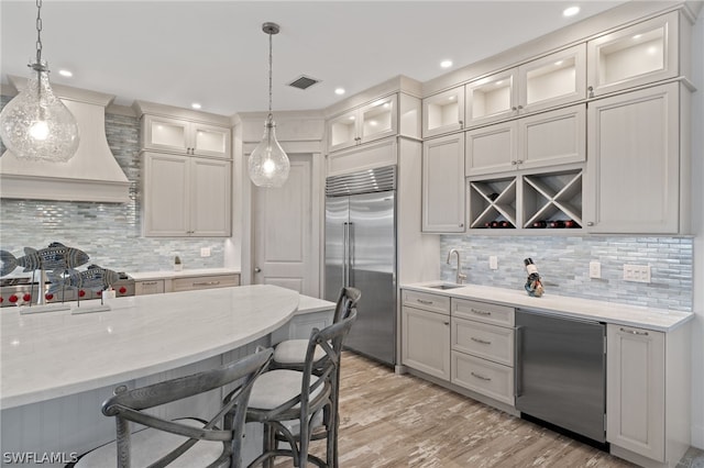 kitchen with decorative light fixtures, light wood-type flooring, backsplash, custom range hood, and built in fridge