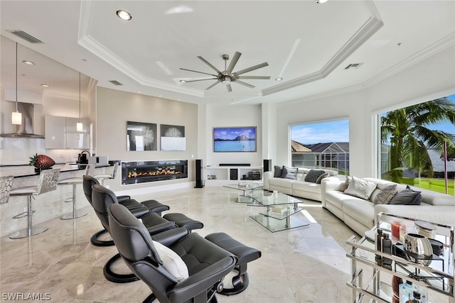 tiled living room with ornamental molding, ceiling fan, and a tray ceiling