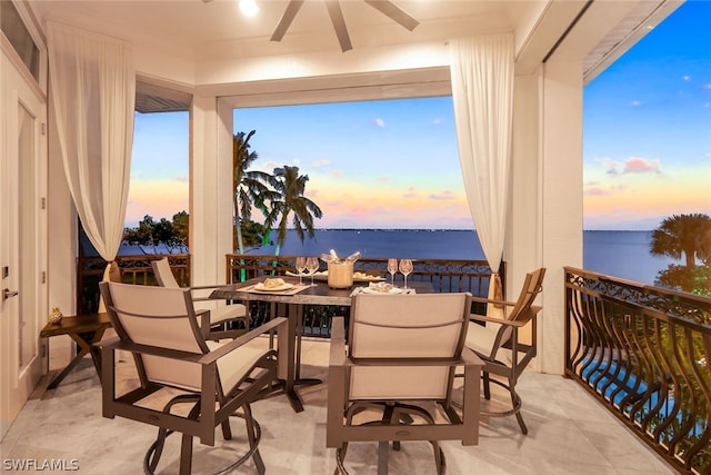 patio terrace at dusk featuring ceiling fan, a water view, and a balcony