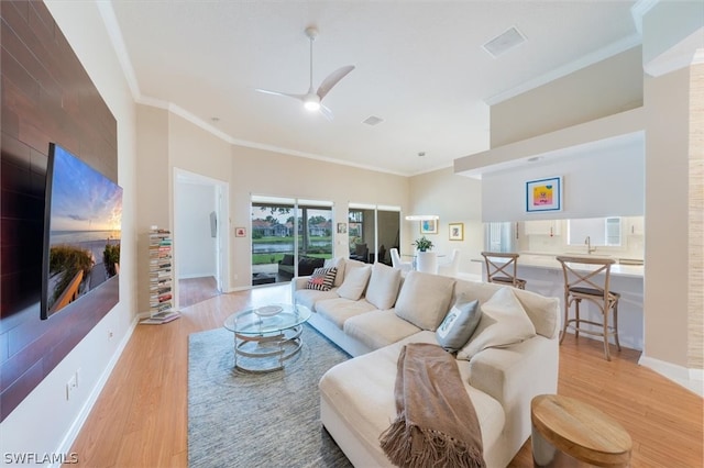 living room with ceiling fan, sink, crown molding, and light hardwood / wood-style flooring