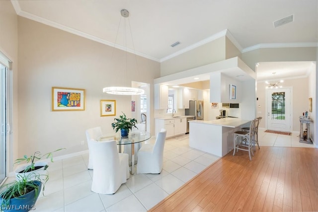 dining room featuring sink, light wood-type flooring, crown molding, and a chandelier