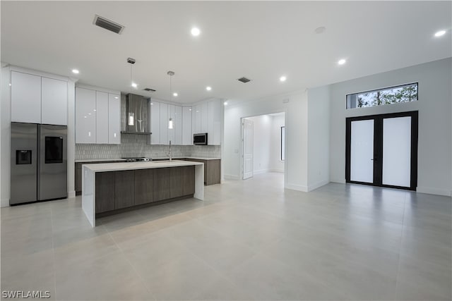 kitchen featuring pendant lighting, white cabinetry, appliances with stainless steel finishes, wall chimney range hood, and an island with sink