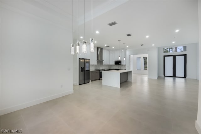 kitchen featuring a center island, wall chimney range hood, white cabinetry, hanging light fixtures, and stainless steel appliances