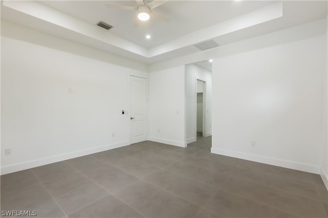 unfurnished room featuring dark tile flooring, ceiling fan, and a raised ceiling