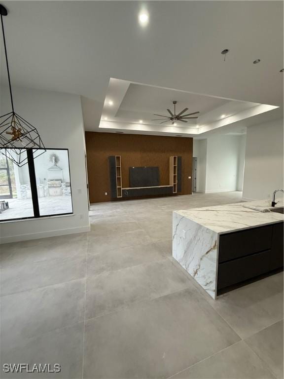 kitchen with hanging light fixtures, light stone countertops, ceiling fan, and a tray ceiling