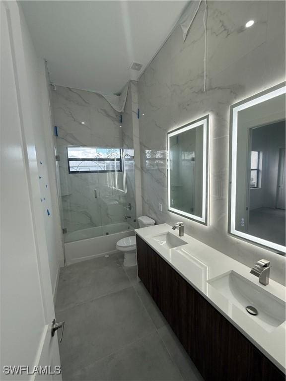 full bathroom featuring toilet, vanity, bath / shower combo with glass door, and tile walls