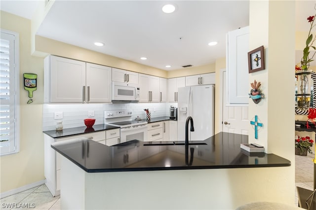 kitchen with light tile patterned floors, white appliances, white cabinetry, backsplash, and kitchen peninsula