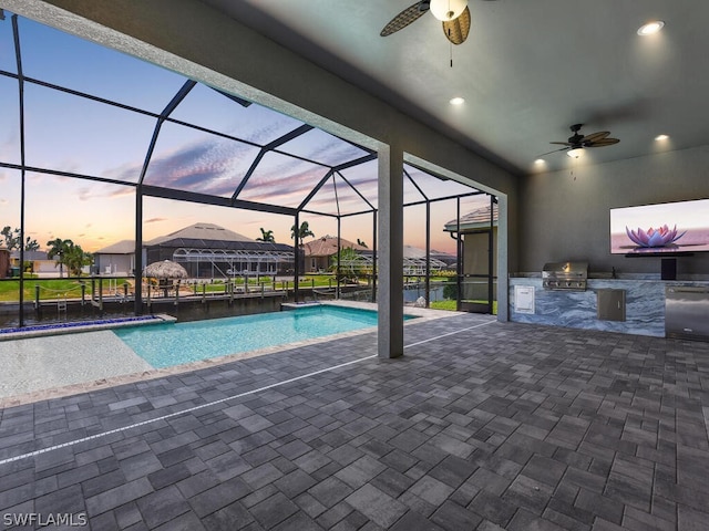 pool at dusk featuring glass enclosure, area for grilling, a patio area, and a grill