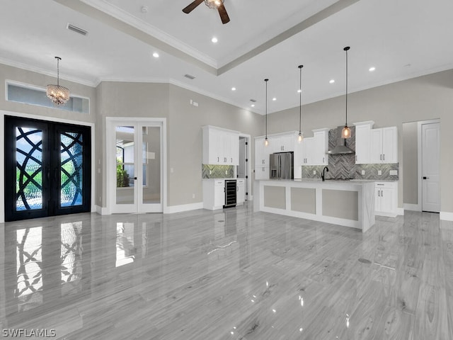 unfurnished living room featuring sink, french doors, wine cooler, ceiling fan with notable chandelier, and ornamental molding