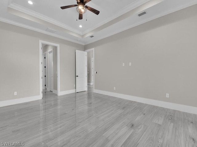 empty room featuring a tray ceiling, ceiling fan, ornamental molding, and light hardwood / wood-style floors