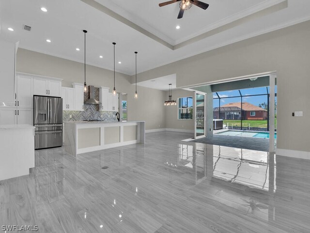 kitchen with pendant lighting, white cabinets, wall chimney range hood, ceiling fan, and stainless steel fridge