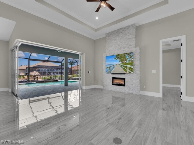 living room featuring light wood-type flooring, ornamental molding, a raised ceiling, ceiling fan, and a fireplace