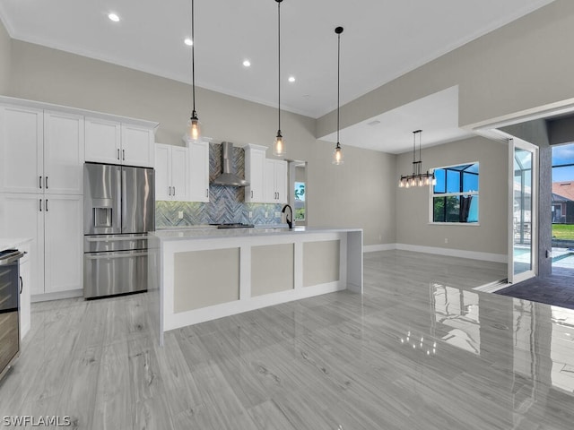 kitchen with wall chimney exhaust hood, a kitchen island with sink, stainless steel fridge with ice dispenser, white cabinetry, and hanging light fixtures