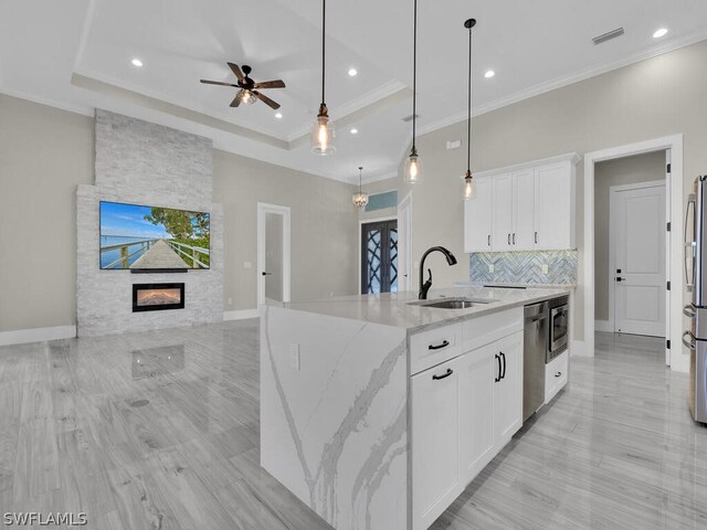 kitchen featuring light stone counters, pendant lighting, a fireplace, white cabinets, and a center island with sink