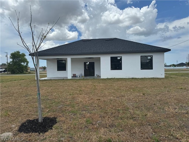 back of house featuring ceiling fan, roof with shingles, a lawn, and stucco siding