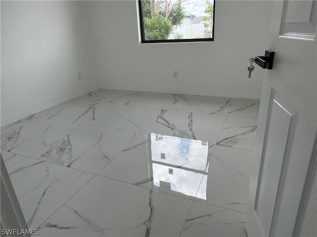 unfurnished room featuring marble finish floor and baseboards