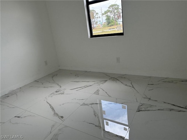 spare room featuring marble finish floor and baseboards