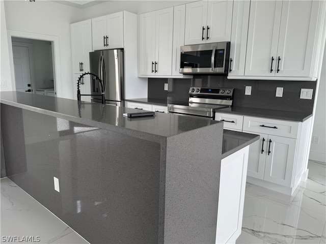 kitchen with an island with sink, light tile floors, sink, white cabinetry, and appliances with stainless steel finishes