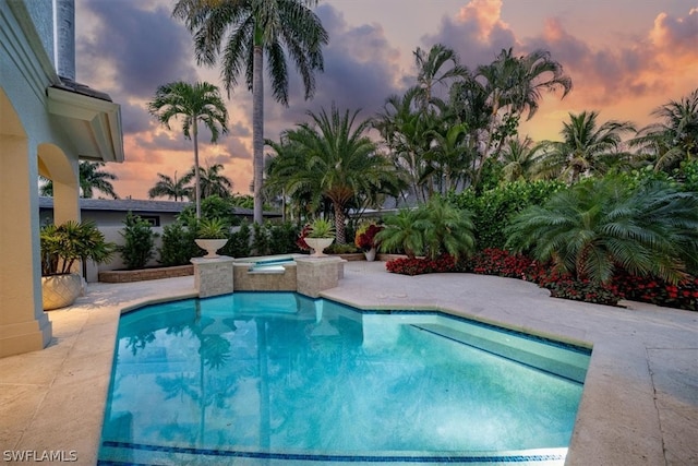 pool at dusk with a patio and an in ground hot tub