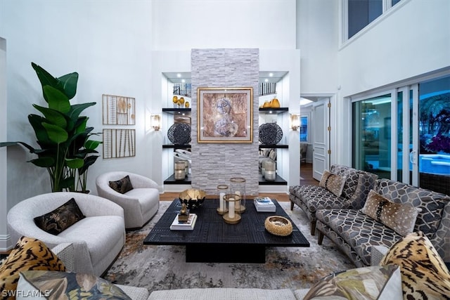 living room featuring wood-type flooring, a high ceiling, and a stone fireplace