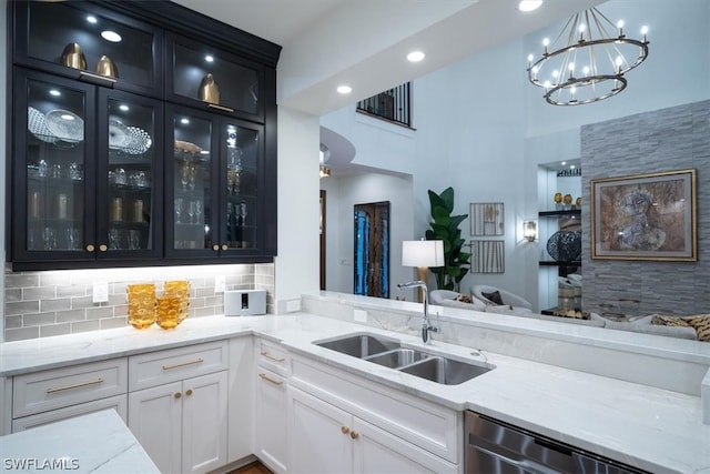 kitchen featuring light stone countertops, tasteful backsplash, white cabinets, sink, and stainless steel dishwasher