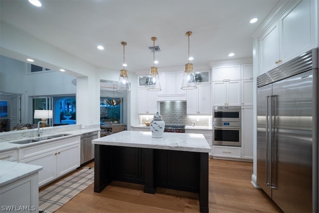 kitchen with backsplash, stainless steel appliances, sink, light stone counters, and light hardwood / wood-style floors