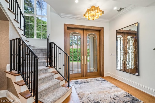 foyer entrance featuring french doors, hardwood / wood-style flooring, a chandelier, and ornamental molding