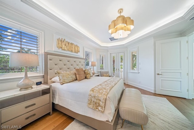 bedroom with french doors, crown molding, light wood-type flooring, and a tray ceiling