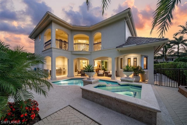 back house at dusk with a patio, a pool with hot tub, and a balcony