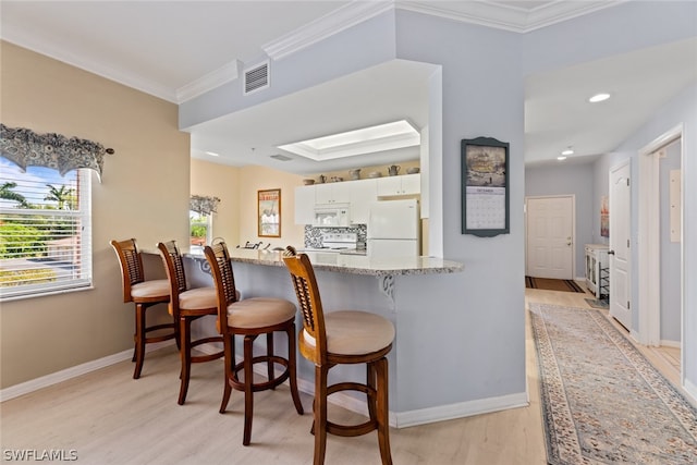 kitchen featuring a kitchen breakfast bar, light hardwood / wood-style flooring, white appliances, light stone counters, and white cabinetry