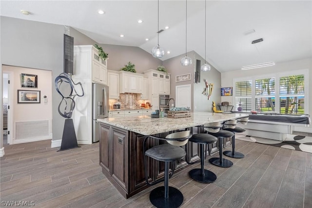 kitchen featuring hanging light fixtures, light stone counters, a spacious island, wood-type flooring, and a breakfast bar