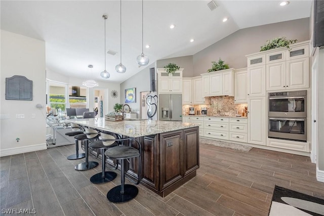 kitchen featuring stainless steel appliances, vaulted ceiling, a large island with sink, pendant lighting, and dark hardwood / wood-style floors