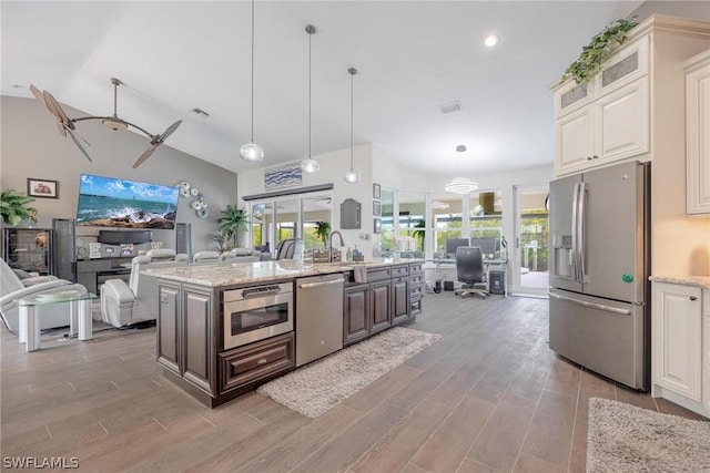 kitchen with ceiling fan, hanging light fixtures, stainless steel appliances, light hardwood / wood-style flooring, and an island with sink