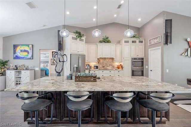 kitchen with dark wood-type flooring, pendant lighting, stainless steel appliances, and a kitchen breakfast bar