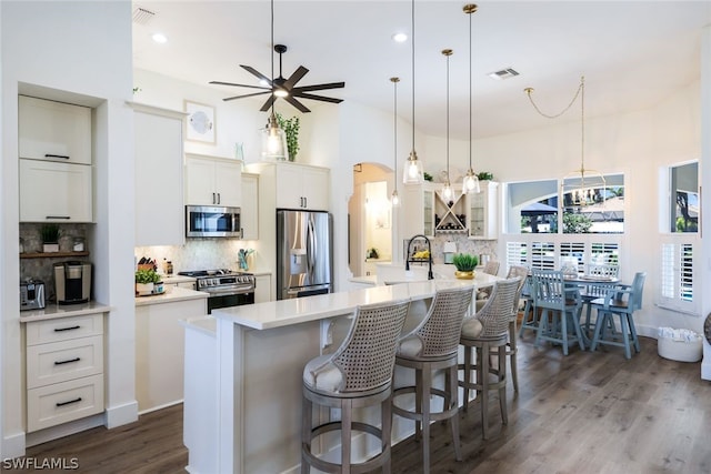 kitchen featuring decorative light fixtures, backsplash, hardwood / wood-style floors, an island with sink, and appliances with stainless steel finishes