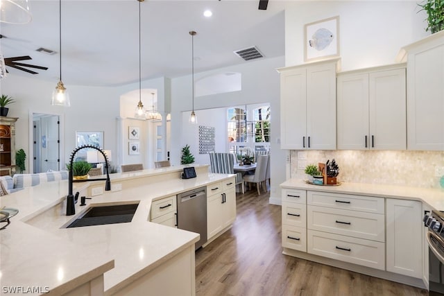 kitchen with white cabinetry, light wood-type flooring, stainless steel dishwasher, ceiling fan with notable chandelier, and pendant lighting