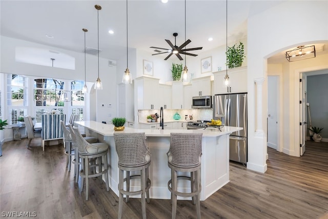 kitchen with dark hardwood / wood-style floors, stainless steel appliances, a center island with sink, hanging light fixtures, and tasteful backsplash