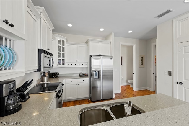 kitchen with light stone countertops, light hardwood / wood-style flooring, stainless steel appliances, sink, and white cabinets