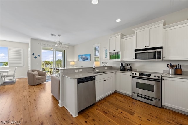 kitchen with ceiling fan, kitchen peninsula, stainless steel appliances, light wood-type flooring, and sink