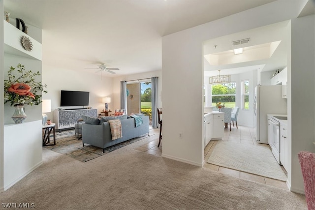 living room featuring a tray ceiling, light colored carpet, and ceiling fan with notable chandelier