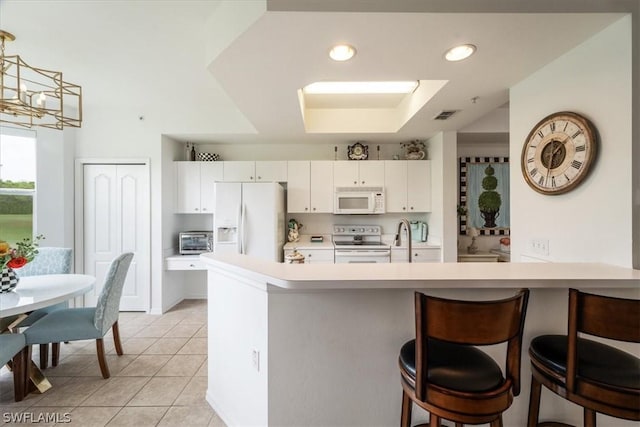 kitchen with pendant lighting, white cabinets, a kitchen bar, light tile patterned floors, and white appliances