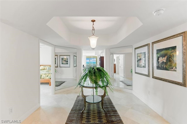 hallway with light tile floors and a tray ceiling